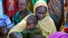 FILE - A mother and her child sit with other families at a camp for internally displaced people in Dougi, Cameroon. 