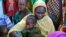 FILE - A mother and her child sit with other families at a camp for internally displaced people in Dougi, Cameroon. 