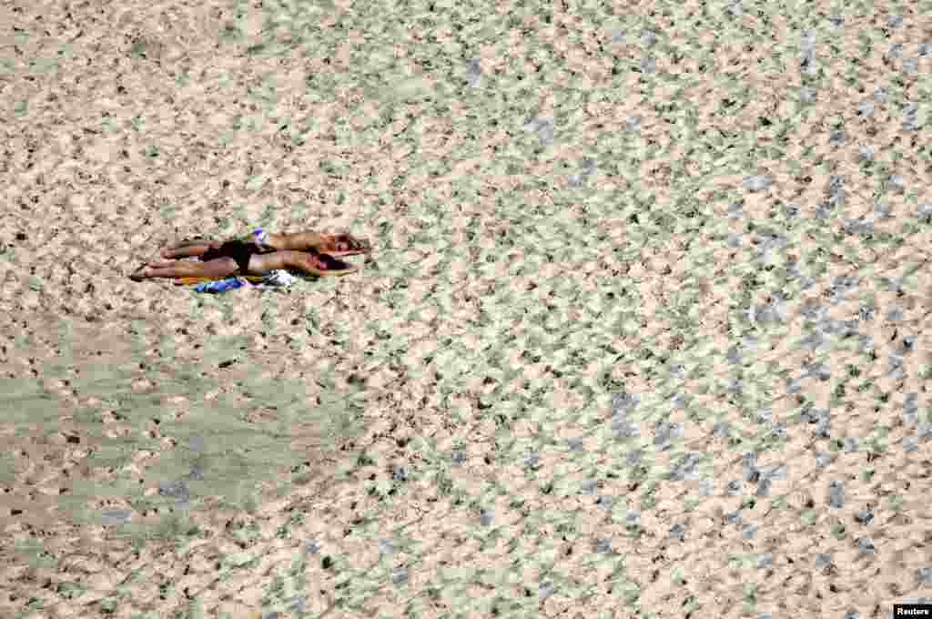 Dua orang perempuan berjemur di pantai Bronte pada siang hari yang cerah di Sydney, Australia.