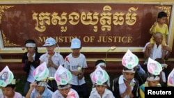 រូបឯកសារ៖ ក្រុមកុមារដែល​ជាកូនៗ​របស់​ស្ត្រី​ដែល​ត្រូវបាន​ចាប់ខ្លួន​ក្នុង​ការប៉ះទង្គិច​ជាមួយ​ប៉ូលិស​ក្នុង​អំឡុងពេល​នៃការបណ្តេញចេញ​ដោយ​បង្ខំនៅ​តំបន់​បឹងកក់​ពាក់​រូបថត​ម្តាយ​នៅលើ​ថ្ងាស នៅក្នុង​ការតវ៉ា​មួយ​នៅមុខ​ក្រសួង​យុត្តិធម៌​ក្នុងរាជធានី​ភ្នំពេញ​កាលពី​ថ្ងៃទី៣១ ខែឧសភា ឆ្នាំ ២០១២។