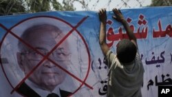 Seorang demonstran memasang poster Ahmed Shafiq dengan menyamakan Shafiq sebagai kepanjangan tangan dari rejim Mubarak dalam protes hari Kamis (14/6). 