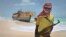 FILE - A masked and armed Somali pirate stands near a fishing vessel.