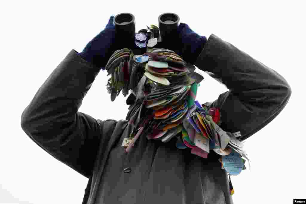 Seorang penonton balapan kuda, mengenakan semua lencana dari balapan sebelumnya, menggunakan teropong selama Festival balap kuda Cheltenham di Gloucestershire, Inggris Barat.