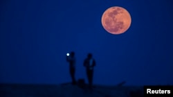 FILE - A man takes a picture of the moon rising during a lunar eclipse, in a suburb of Shanghai, April 15, 2014. 