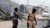 FILE - Somali police walk around the scene of an explosion near the entrance of the airport in Mogadishu, Feb. 13, 2014.