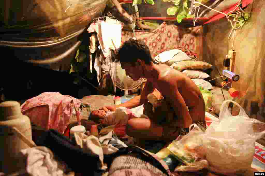 A man feeds his two-month old twins in a tent erected atop a tombstone at the North Cemetery where many victims of the country&#39;s war on drugs are buried, in Manila, Philippines.