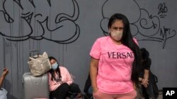 FILE -Passengers wearing face masks wait outside a bus terminal, in Lima, Peru, Jan. 30, 2021. 
