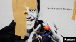 资料照：俄罗斯圣彼得堡的一个工人在涂抹掉俄罗斯反对派领导人阿列克谢·纳瓦尔尼（Aleksey Navalny）的画像，画像旁写着“新时代的英雄”。（2021年4月28日）