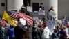 FILE - Law enforcement officers look on through Ohio Statehouse doors as people rally outside to protest the stay-at-home order in Columbus, Ohio, April 20, 2020.