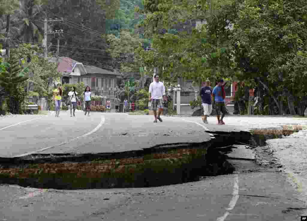 Warga berjalan di atas jalan layang yang rusak di kota Loboc, provinsi Bohol di Filipina bagian tengah (16/10). (AP/Bullit Marquez)