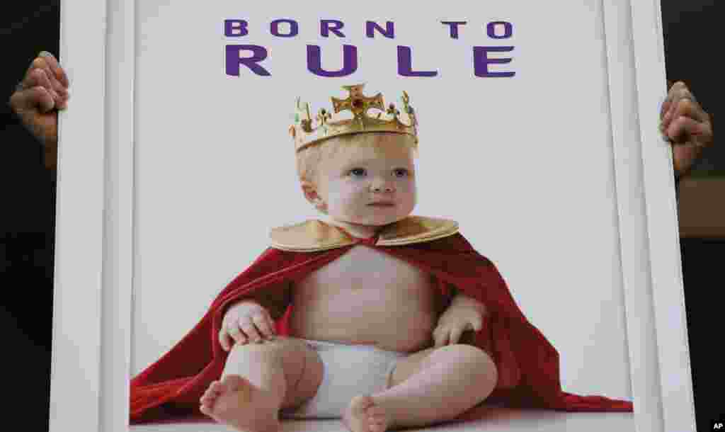 Seorang pegawai perusahaan permainan berpose untuk media dengan poster bertuliskan &quot;Lahir untuk Berkuasa&quot; di luar Rumah Sakit St. Mary&#39;s di London. (AP Photo/Lefteris Pitarakis)