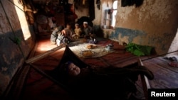 An ethnic Hazara child sleeps as the rest of the family eat a meal in their home in Turkman camp in Nowshera, Pakistan.