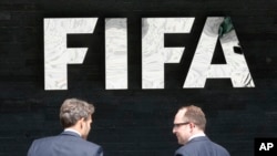 Deux hommes se parlent devant le logo de la FIFA au siège de la FIFA, à Zurich, en Suisse, le mercredi 27 mai 2015, après que les procureurs suisses aient engagé des poursuites pénales contre la corruption «rampante, systémique et profondément enracinée». (Photo AP / Michael Probst)