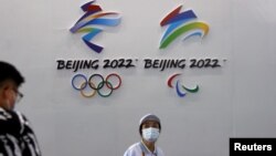 一名戴着口罩的妇女走过北京的国际服务贸易交易会悬挂的2022年冬季奥运会和冬季残奥会标识。（2021年9月3日）
