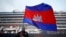 FILE - A Cambodian man holds his national flag in front of the MS Westerdam, owned by Holland America Line, dockked at the port of Sihanoukville, Cambodia, Friday, Feb. 14, 2020.