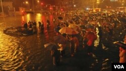 在北京广渠门立交桥附近，救援人员和居民站在一旁观望一辆从街道积水中被拖出的小汽车(7月21日) 