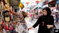 In this Wednesday, July 3, 2019 photo, a woman inspects a headscarf at a market in downtown Tehran, Iran. A few daring women in Iran's capital have been taking off their mandatory headscarves, or hijabs, in public.