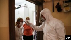 FILE - A contact tracer with Turkey's Health Ministry's coronavirus contact-tracing team, clad in white protective gear, mask and face shield, swabs a woman who had been experiencing COVID-19 symptoms, in Istanbul, May 15, 2020.