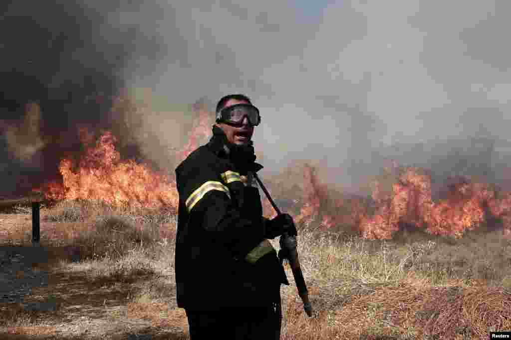 Seorang petugas pemadam kebakaran berteriak kepada seorang rekannya saat ia mencoba memadamkan kebakaran di wilayah Markopoulo, beberapa kilometer di barat daya Athena, Yunani. 