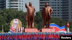 Les gens portent des drapeaux devant les statues du fondateur de la Corée du Nord, Kim Il Sung, à gauche, et le défunt leader Kim Jong Il lors d'un défilé militaire marquant le 70e anniversaire de la fondation de la Corée du Nord à Pyongyang, en Corée du Nord, le 9 septembre 2018.