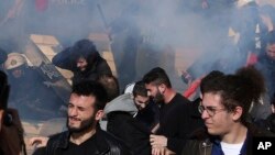 Police fire tear gas as protesters try to avoid it on the steps of parliament during a rally against a new austerity bill that will limit the right to strike and speed up property foreclosures, in Athens, Jan. 12, 2018.