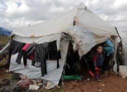FILE - An internally displaced Syrian child from Idlib stands outside a tent in Azaz, Syria, Feb. 22, 2020.
