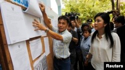 Thai Prime Minister Yingluck Shinawatra (R) checks a list of voters' names before voting at a polling station in Bangkok, March 30, 2014.