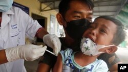 A young boy, held by his father, reacts as he receives a second dose of the Sinovac's COVID-19 vaccine at a Krang Thnung health center outside Phnom Penh, Cambodia, Monday, Nov. 15, 2021. (AP Photo/Heng Sinith)