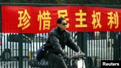 资料照：一名男子在北京街头骑车路过一条敦促市民”珍惜民主权利“的标语横幅。（2003年11月4日）