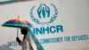 A Congolese man carries an umbrella decorated with a United Nations flag as Muslim and Christian refugees protest together outside the head office of the United Nations refugee agency in Bangui, Central African Republic, Jan. 6, 2014.