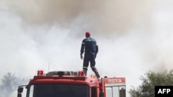 Seorang petugas pemadam kebakaran memperhatikan asap yang mengepul dalam kebakaran yang melanda wilayah Kitsi, di pinggiran selatan Athena, pada 19 Juni 2024. (Foto: Sotiris Dimitropoulos/Eurokinissi/AFP)