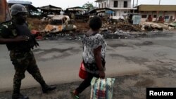 FILE - A woman walks past a Cameroonian elite Rapid Intervention Battalion (BIR) member in the city of Buea in the anglophone southwest region, Cameroon, Oct. 4, 2018.