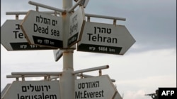 تصویر یک سرباز اسرائیلی در پس زمینه چند تابلو دیده می شود که فاصله تا شهرهای مختلف در خاورمیانه را از یک پاسگاه نظامی در منطقه تازه الحاق شده به اسرائیل در بلندی های جولان نشان می دهد. ۲۸ نوامبر ۲۰۲