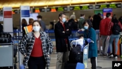 Travelers cover their faces with masks as they wait to drop their luggage at the Los Angeles International Airport.