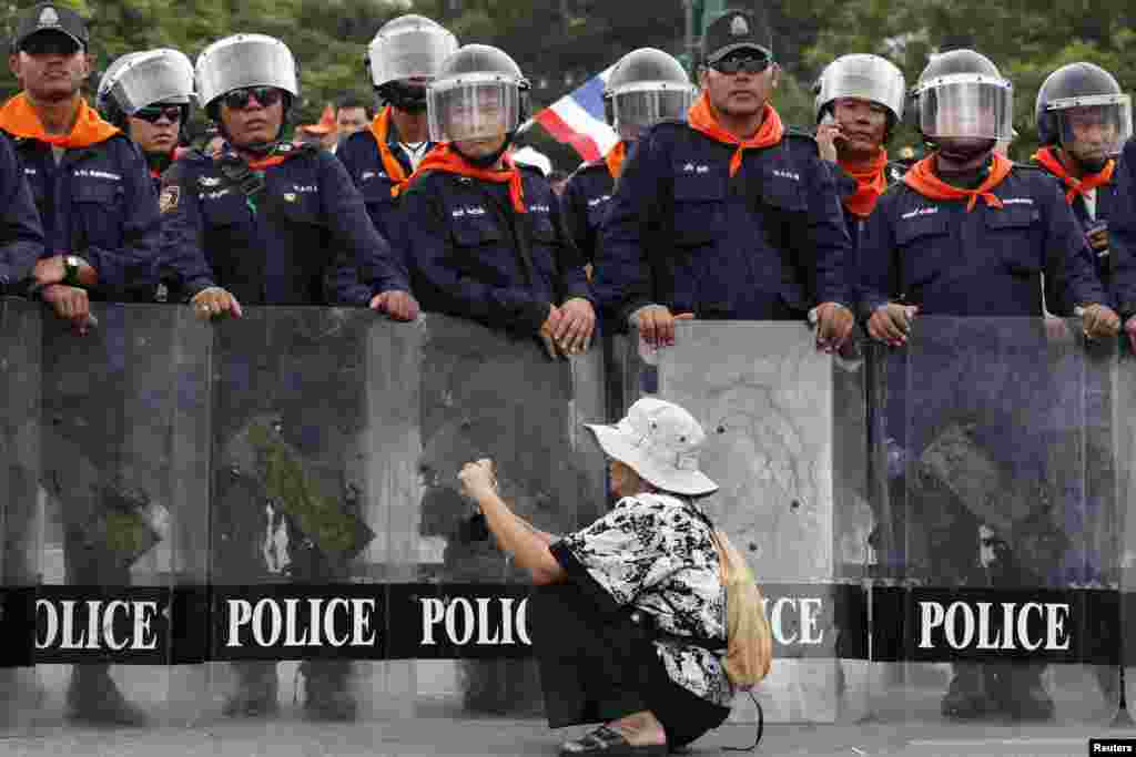 Seorang wanita mengambil gambar di depan para polisi yang menjaga demonstrasi anti RUU amnesti, di kawasan kantor pemerintahan di Bangkok, Thailand.