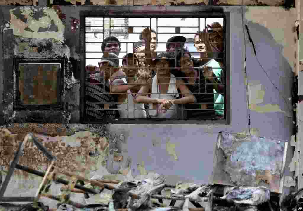 Para penghuni LP Tanjung Gusta mengintip dari balik kantor yang terbakar (12/7) menyusul kerusuhan di penjara itu sehari sebelumnya. (AP/Binsar Bakkara)