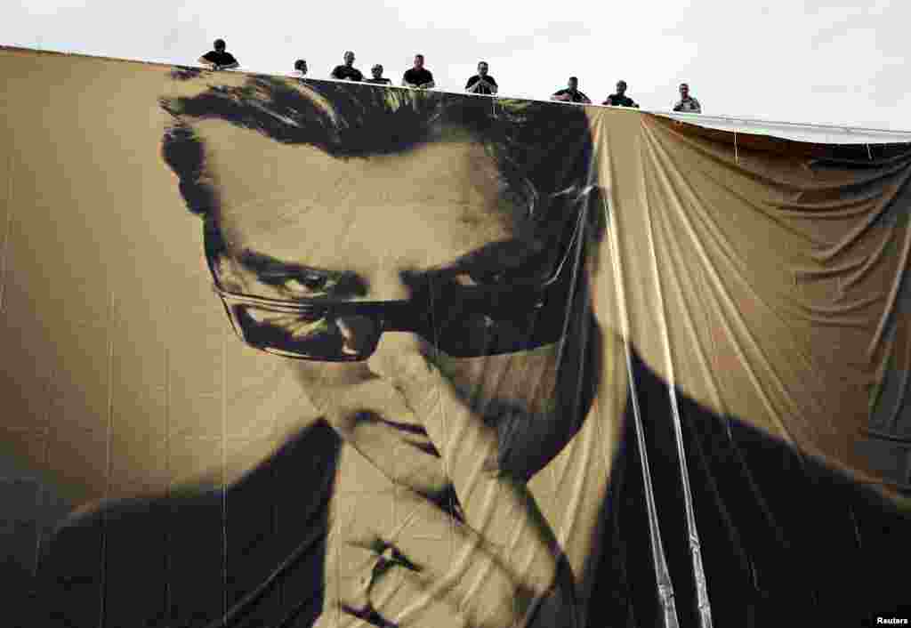 Workers set up a giant canvas of the official poster of the 67th Cannes Film Festival featuring actor Marcello Mastroianni on the Festival Palace in Cannes.