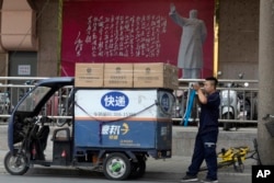 2018年6月27日，北京的一幅毛泽东像和毛泽东诗词牌匾下面，快递员正准备送货。