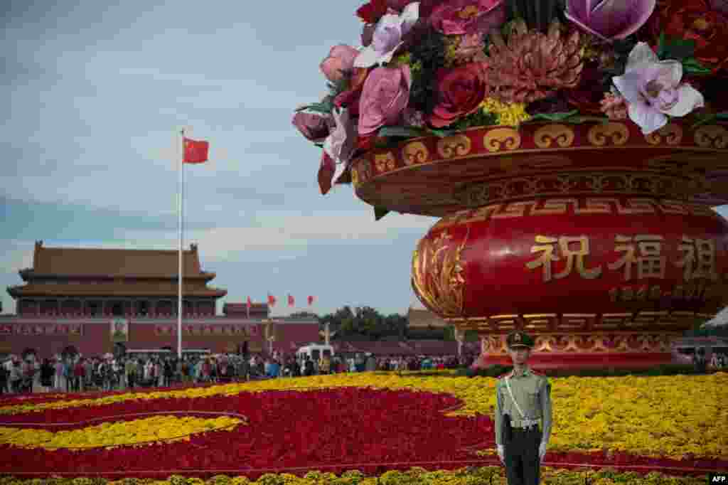 Seorang tentara paramiliter berdiri di depan karangan bunga raksasa di Lapangan Tiananmen menjelang peringatan Hari Nasional China di Beijing. (AFP/Nicolas Asfouri)