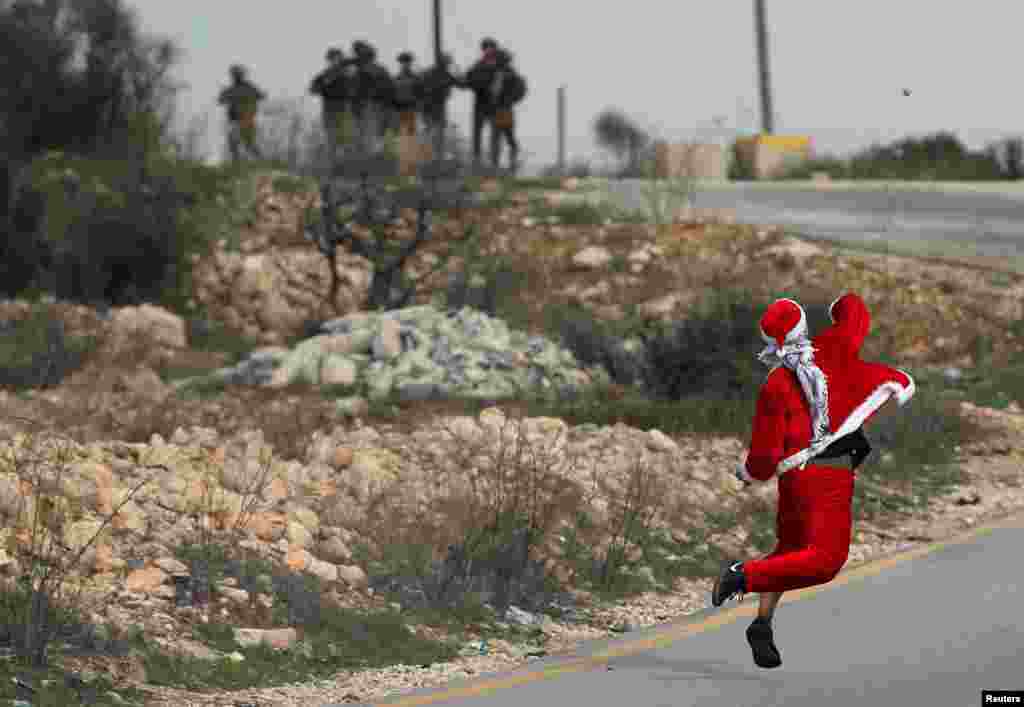 បាតុករ​ប៉ាឡេស្ទីន​ម្នាក់​ស្លៀក​ពាក់​ជា​ Santa Claus គប់​ថ្ម​ទៅកាន់​ទាហាន​អ៊ីស្រាអែល​អំឡុង​ការ​ប៉ះទង្គិច​ប្រឆាំង​នឹង​ការ​សម្រេចចិត្ត​របស់​ប្រធានាធិបតី​សហរដ្ឋអាមេរិក​ត្រាំ​ក្នុង​ការ​ទទួល​ស្គាល់​​ទីក្រុង​ Jerusalem ជា​រដ្ឋធានី​របស់​អ៊ីស្រាអែល​នៅ​ទីក្រុង​ Ramallah នៃ​តំបន់ West Bank។