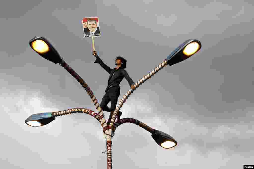 Seorang pendukung presiden terguling Mohamed Morsi memegang fotonya sambil berdiri di atas lampu jalanan dalam demonstrasi di Sana&#39;a, Yaman, untuk menunjukkan solidaritas pada teman-teman mereka di Mesir.