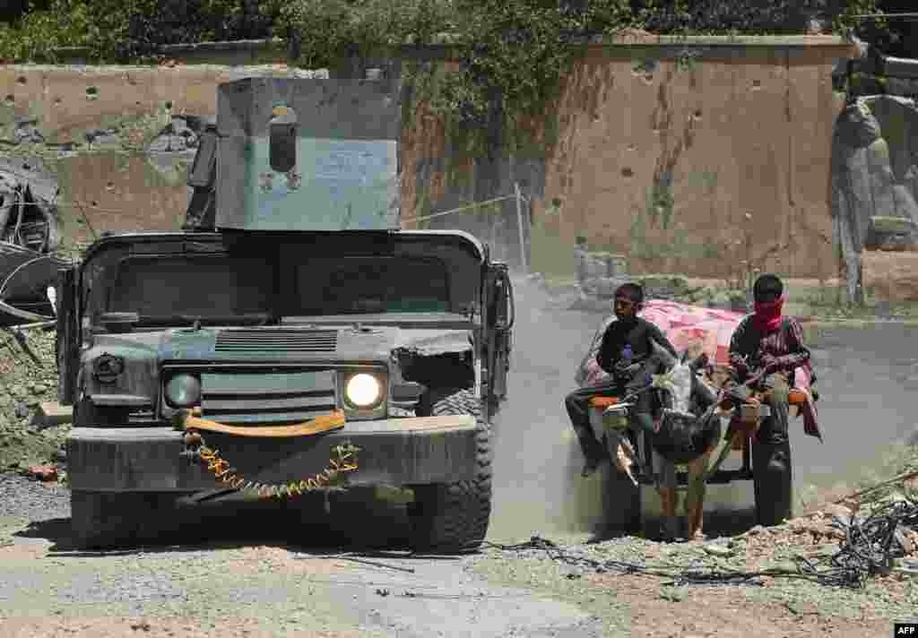 Sebuah kendaraan militer Irak melintas dekat anak-anak lelaki pengungsi Irak yang kembali ke rumahnya di kawasan Oreibi di Mosul Barat setelah pasukan pemerintah berhasil merebut kawasan tersebut dari kelompok Islamic State (IS).