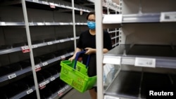 一名戴口罩的新加坡妇女星期六（2月8日）在商店购物。货架上的方便面和罐头食品似乎已被抢购一空。 