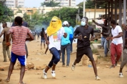FILE - Demonstrator opposed to Ivory Coast President Alassane Ouattara running for a third term confront riot police in Abidjan, Aug. 13, 2020.