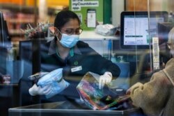 Kasir di sebuah supermarket di Auckland, Selandia Baru, membantu pelanggan memasukkan barang belanjaannya ke dalam tas, Selasa, 17 Agustus 2021. (AP)