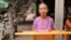 Im Chaem stands behind a podium holding her Bible in front of her home in O'Angre village, Anlong Veng district, Oddar Meanchey province, Cambodia. (Courtesy photo of Pastor Touch Chanthou)