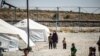 FILE - A woman clad in a mask due to the COVID-19 pandemic walks next to a child by tents at Camp Roj, housing people who were relocated from al-Hol camp, in Syria's northeastern Hasakah province, Sept. 30, 2020.