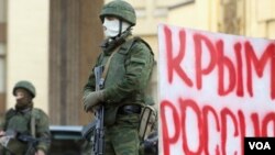 Pria berseragam dan bersenjata tanpa tanda-tanda militer berjaga-jaga di gedung parlemen Krimea, Ukraina, dekat spanduk bertuliskan "Krimea Rusia".