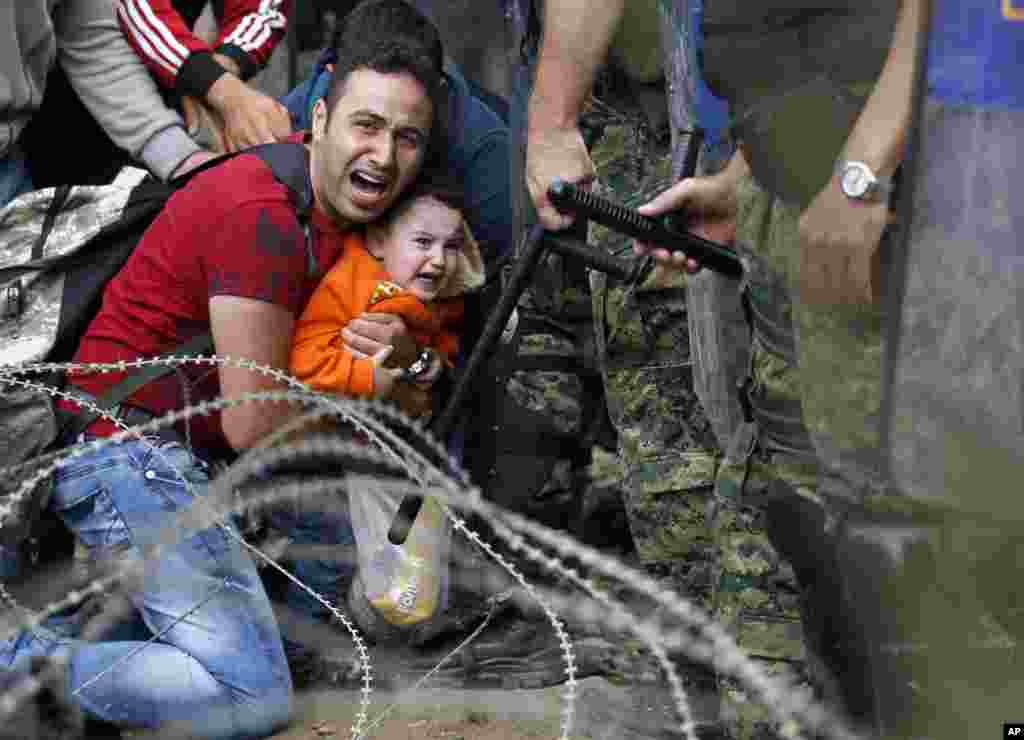 A migrant man holding a boy react as they are stuck between Macedonian riot police officers and migrants during a clash near the border train station of Idomeni, northern Greece, as they wait to be allowed by the Macedonian police to cross the border from Greece to Macedonia, Aug. 21, 2015.