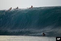 Surfers paddle over the top of a wave in Teahupo'o, Tahiti, French Polynesia, Sunday, Jan. 13, 2024. (AP Photo/Daniel Cole)